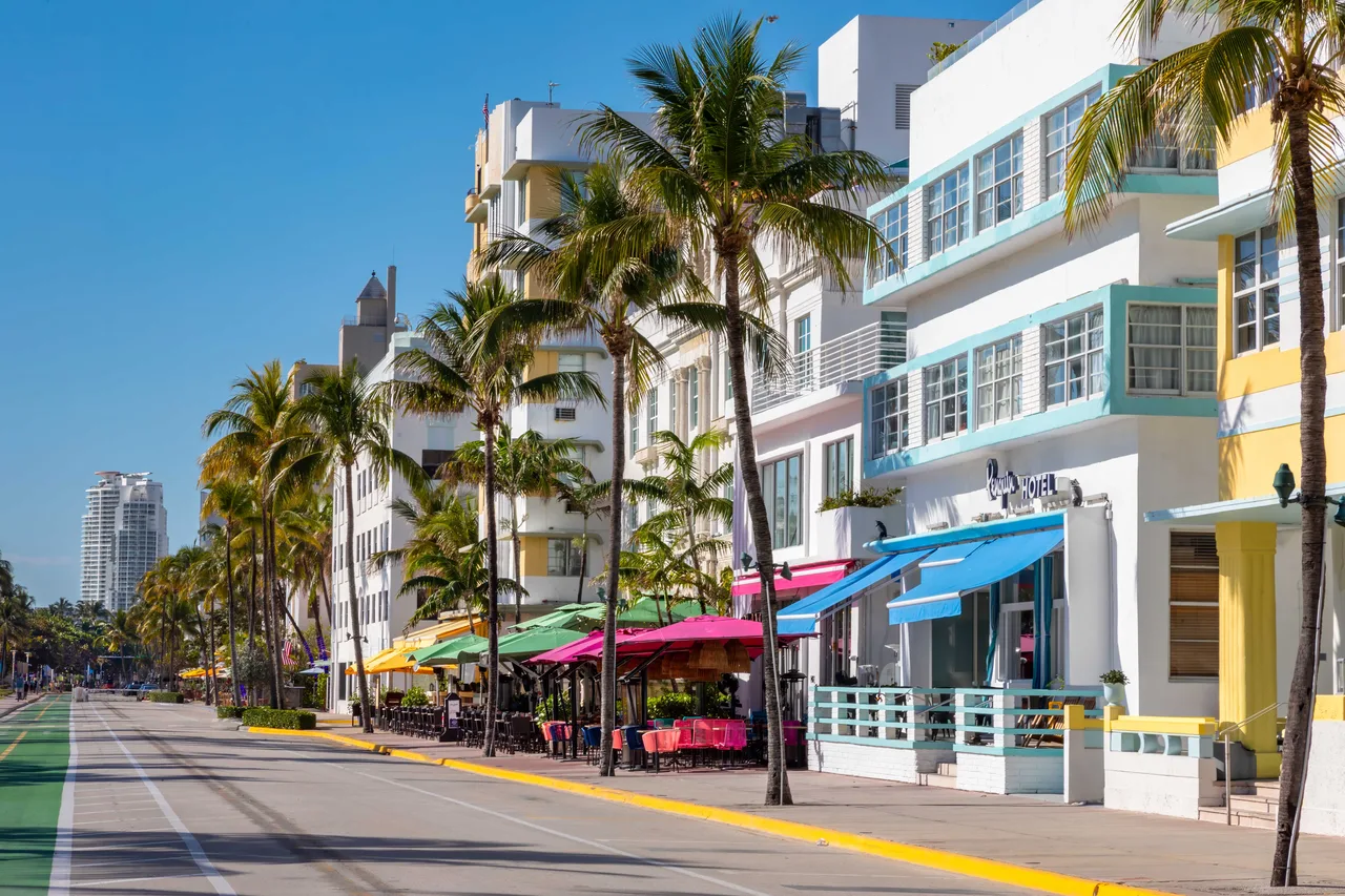 Façades pastel Art déco d'Ocean Drive en plein jour, palmiers et parasols colorés